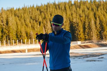 Image showing Handsome male athlete with cross country skis, taking fresh breath and having break after hard workout training in a snowy forest. Checking smartwatch. Healthy winter lifestyle