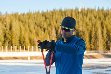 Image showing Handsome male athlete with cross country skis, taking fresh breath and having break after hard workout training in a snowy forest. Checking smartwatch. Healthy winter lifestyle