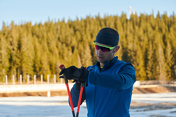 Image showing Handsome male athlete with cross country skis, taking fresh breath and having break after hard workout training in a snowy forest. Checking smartwatch. Healthy winter lifestyle