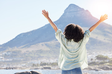 Image showing Woman at beach, arms in air and freedom, back view with mountains and travel, praise and sunshine. Female person outdoor, carefree and adventure, mindfulness and peace with worship in nature