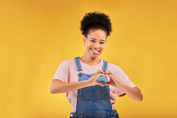Image showing Hands, black woman and sign for a heart, love and portrait of care or support on yellow background in studio. Happy, face and girl with hand gesture for loving, kindness or emoji for caring mindset