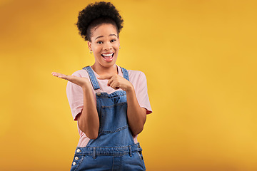 Image showing Portrait, space and a black woman pointing to her palm for the promotion of a product on a yellow background in studio. Smile, advertising or marketing with a happy young female brand ambassador