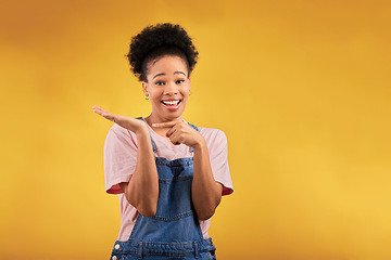 Image showing Portrait, marketing and a black woman pointing to her palm for the promotion of a product on a yellow background in studio. Smile, advertising or space with a happy young female brand ambassador