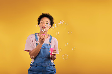 Image showing Blowing bubbles, woman and fun in studio while playful for birthday or party celebration. Black female model person with liquid soap, natural beauty and fashion on a yellow background with space