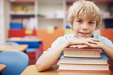 Image showing So much to learn. A happy young boy sitting at his desk and leaning his chin on a stack of books.