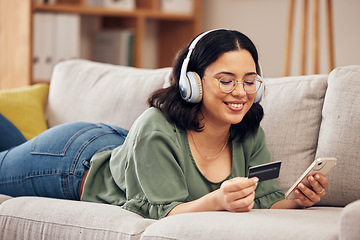 Image showing Woman, credit card and phone on sofa, home and headphones with smile, online shopping or payment on web. Girl, smartphone and fintech app for cybersecurity, discount and deal with e commerce store