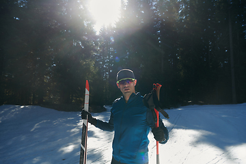 Image showing Portrait handsome male athlete with cross country skis in hands and goggles, training in snowy forest. Healthy winter lifestyle concept.