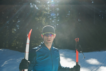 Image showing Portrait handsome male athlete with cross country skis in hands and goggles, training in snowy forest. Healthy winter lifestyle concept.