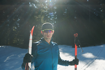 Image showing Portrait handsome male athlete with cross country skis in hands and goggles, training in snowy forest. Healthy winter lifestyle concept.