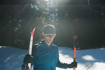 Image showing Portrait handsome male athlete with cross country skis in hands and goggles, training in snowy forest. Healthy winter lifestyle concept.