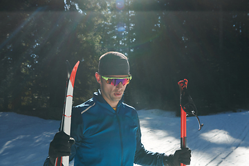 Image showing Portrait handsome male athlete with cross country skis in hands and goggles, training in snowy forest. Healthy winter lifestyle concept.