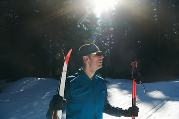 Image showing Portrait handsome male athlete with cross country skis in hands and goggles, training in snowy forest. Healthy winter lifestyle concept.