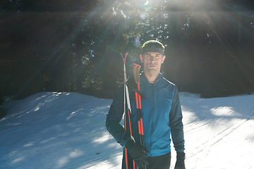 Image showing Portrait handsome male athlete with cross country skis in hands and goggles, training in snowy forest. Healthy winter lifestyle concept.