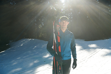 Image showing Portrait handsome male athlete with cross country skis in hands and goggles, training in snowy forest. Healthy winter lifestyle concept.