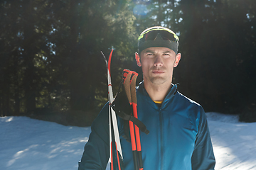 Image showing Portrait handsome male athlete with cross country skis in hands and goggles, training in snowy forest. Healthy winter lifestyle concept.