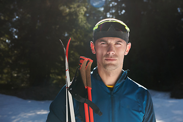 Image showing Portrait handsome male athlete with cross country skis in hands and goggles, training in snowy forest. Healthy winter lifestyle concept.