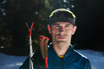 Image showing Portrait handsome male athlete with cross country skis in hands and goggles, training in snowy forest. Healthy winter lifestyle concept.