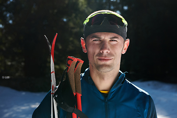 Image showing Portrait handsome male athlete with cross country skis in hands and goggles, training in snowy forest. Healthy winter lifestyle concept.