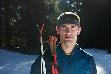 Image showing Portrait handsome male athlete with cross country skis in hands and goggles, training in snowy forest. Healthy winter lifestyle concept.