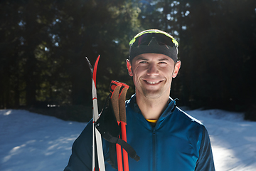 Image showing Portrait handsome male athlete with cross country skis in hands and goggles, training in snowy forest. Healthy winter lifestyle concept.