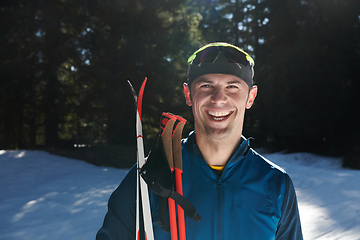 Image showing Portrait handsome male athlete with cross country skis in hands and goggles, training in snowy forest. Healthy winter lifestyle concept.