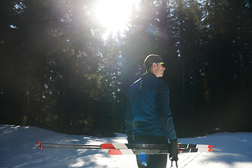 Image showing Portrait handsome male athlete with cross country skis in hands and goggles, training in snowy forest. Healthy winter lifestyle concept.