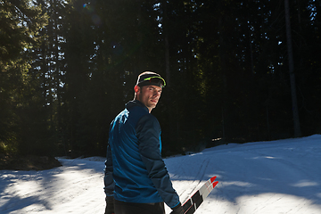 Image showing Portrait handsome male athlete with cross country skis in hands and goggles, training in snowy forest. Healthy winter lifestyle concept.