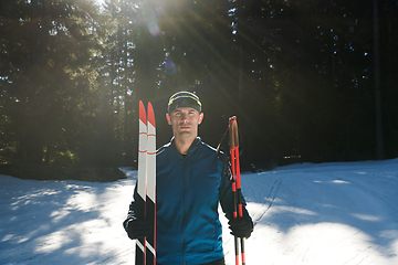 Image showing Portrait handsome male athlete with cross country skis in hands and goggles, training in snowy forest. Healthy winter lifestyle concept.