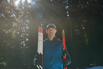 Image showing Portrait handsome male athlete with cross country skis in hands and goggles, training in snowy forest. Healthy winter lifestyle concept.