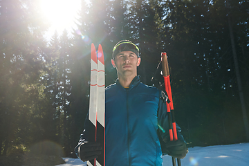 Image showing Portrait handsome male athlete with cross country skis in hands and goggles, training in snowy forest. Healthy winter lifestyle concept.