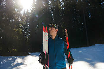 Image showing Portrait handsome male athlete with cross country skis in hands and goggles, training in snowy forest. Healthy winter lifestyle concept.