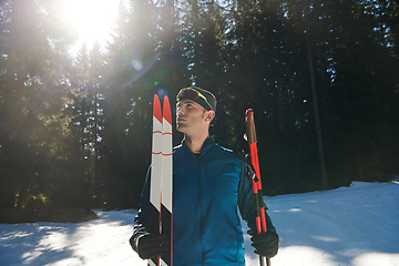 Image showing Portrait handsome male athlete with cross country skis in hands and goggles, training in snowy forest. Healthy winter lifestyle concept.