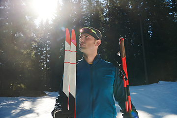 Image showing Portrait handsome male athlete with cross country skis in hands and goggles, training in snowy forest. Healthy winter lifestyle concept.