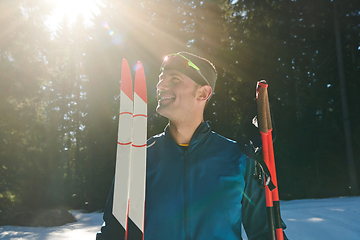 Image showing Portrait handsome male athlete with cross country skis in hands and goggles, training in snowy forest. Healthy winter lifestyle concept.