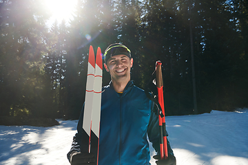 Image showing Portrait handsome male athlete with cross country skis in hands and goggles, training in snowy forest. Healthy winter lifestyle concept.