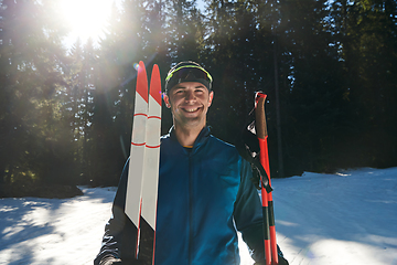 Image showing Portrait handsome male athlete with cross country skis in hands and goggles, training in snowy forest. Healthy winter lifestyle concept.