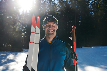 Image showing Portrait handsome male athlete with cross country skis in hands and goggles, training in snowy forest. Healthy winter lifestyle concept.