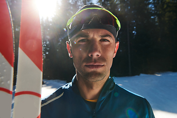 Image showing Portrait handsome male athlete with cross country skis in hands and goggles, training in snowy forest. Healthy winter lifestyle concept.