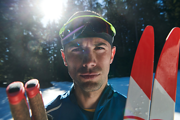 Image showing Portrait handsome male athlete with cross country skis in hands and goggles, training in snowy forest. Healthy winter lifestyle concept.