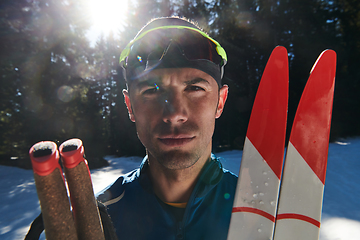 Image showing Portrait handsome male athlete with cross country skis in hands and goggles, training in snowy forest. Healthy winter lifestyle concept.