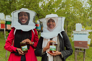 Image showing Portrait of an Arab investors holding a jar of honey in their hands while standing in front of a large honey farm. The concept of investing in small businesses