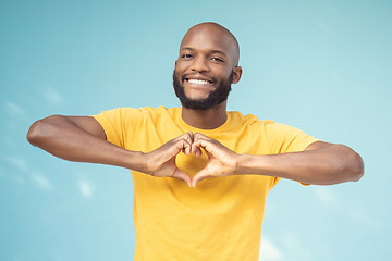 Image showing Hand, heart and portrait of man in studio for love, happy and smile against a blue background space. Emoji, hands and face of male model relax with finger, frame and loving message, gesture and sign