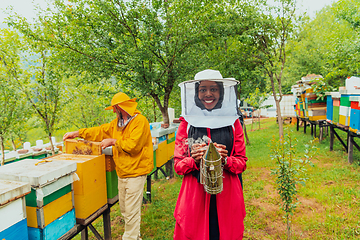 Image showing Portrait of a Muslim African American woman in the beekeeping department of a honey farm holding a jar of honey in her hand