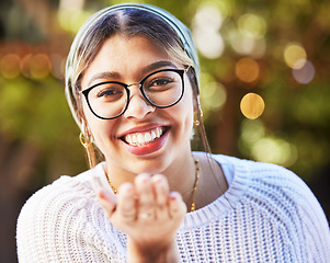 Image showing Portrait, smile and blowing a kiss with a woman on a nature green background for love or romance. Face, glasses and flirt with a happy young female person standing in a garden on valentines day