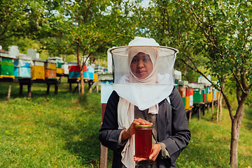 Image showing Portrait of a Muslim African American woman in the beekeeping department of a honey farm holding a jar of honey in her hand