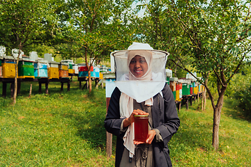 Image showing Portrait of a Muslim African American woman in the beekeeping department of a honey farm holding a jar of honey in her hand