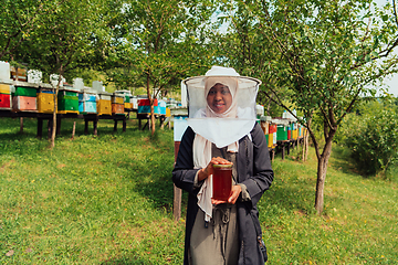 Image showing Portrait of a Muslim African American woman in the beekeeping department of a honey farm holding a jar of honey in her hand