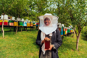 Image showing Portrait of a Muslim African American woman in the beekeeping department of a honey farm holding a jar of honey in her hand