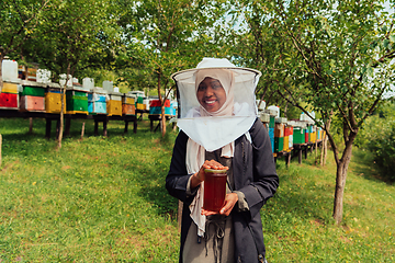 Image showing Portrait of a Muslim African American woman in the beekeeping department of a honey farm holding a jar of honey in her hand