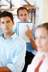 Image showing You mean we have to get up to here. Three colleagues are gathered in an office with one colleague pointing to his notes.